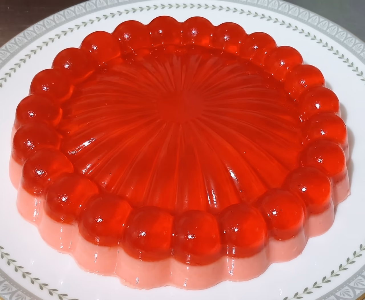 Gelatina roja en molde redondo de perlas sobre un plato blanco